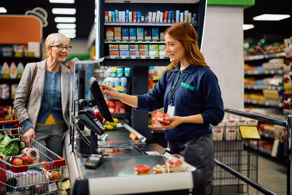 A happy supermarket cashier helping an elderly woman at checkout