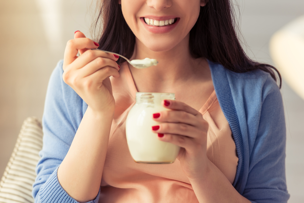 A woman taking a spoonful of yoghurt while holding a cup of yogurt