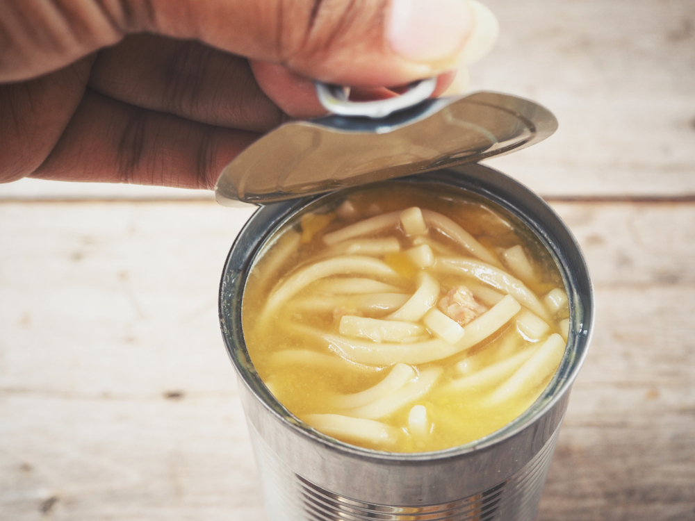 A woman opening a canned chicken noodle soup