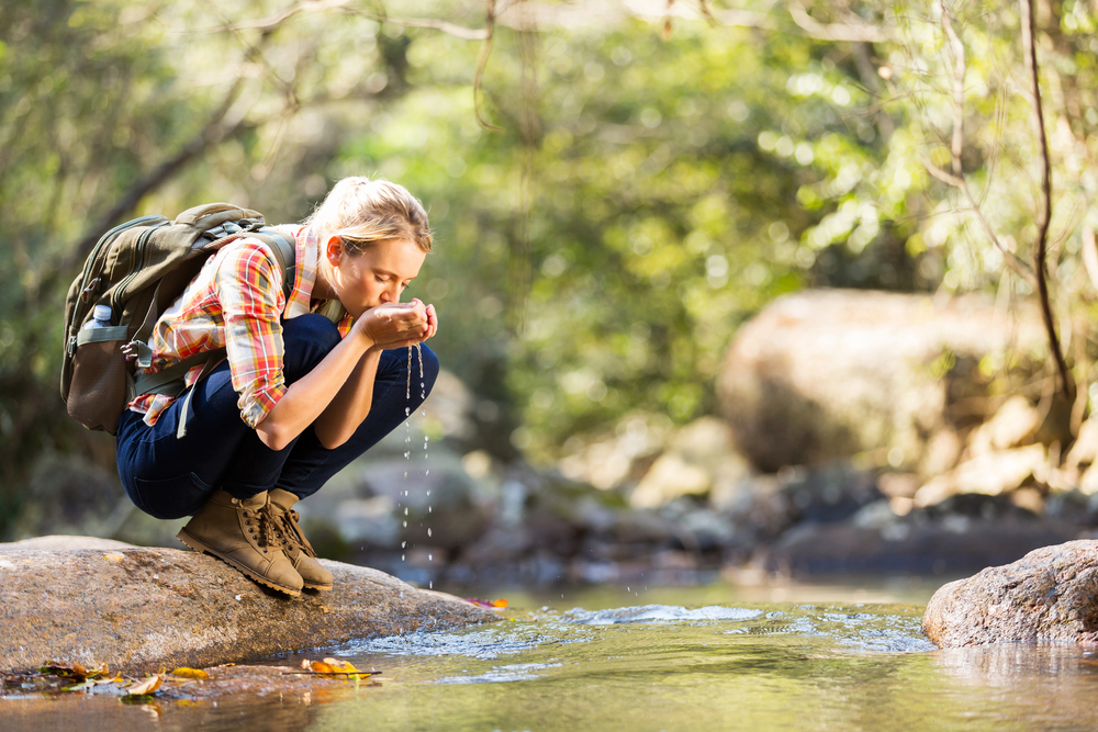 A young female hiker drinking water from a stream with her cupped hands