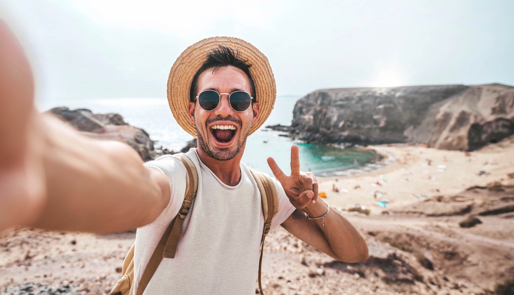 Man giving the peace sign with his fingers and standing at the beach.