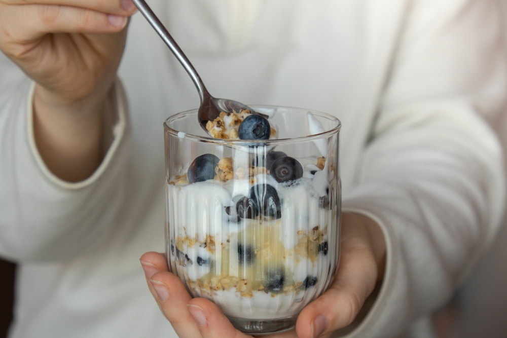 A woman eating breakfast meal of granola with Greek yoghurt and fruits