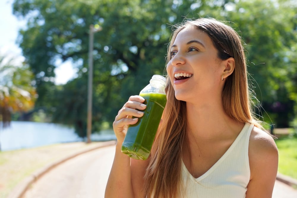 An attractive happy healthy young woman drinking her green juice outside
