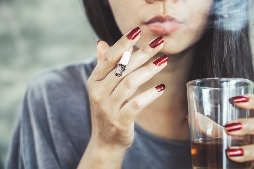 A woman smoking a cigarette while holding a drink