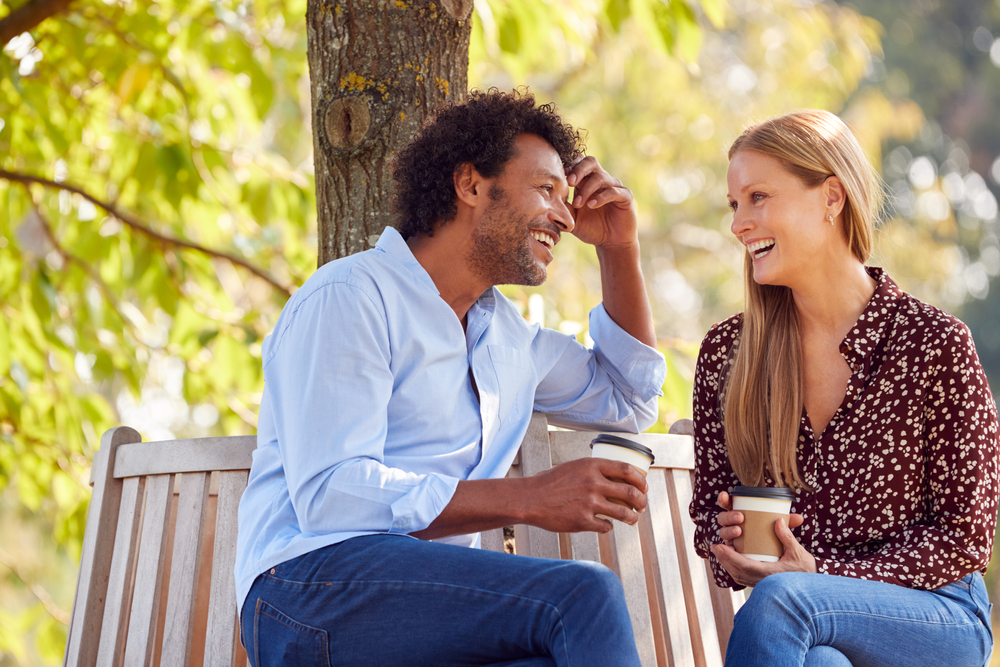 A lovely mature couple sitting on a park bench, talking, laughing and having fun together