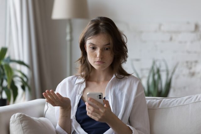 Shocked and confused young woman looking at her phone.
