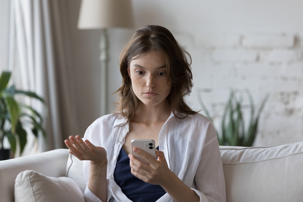 Shocked and confused young woman looking at her phone.