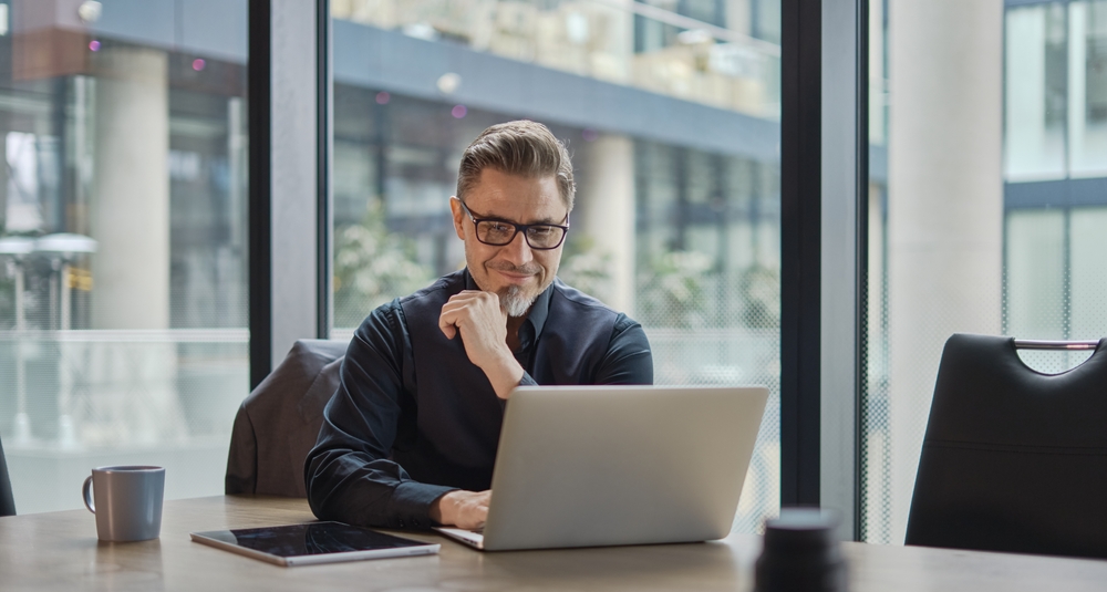 A happy businessman sitting and working at his desk with a laptop