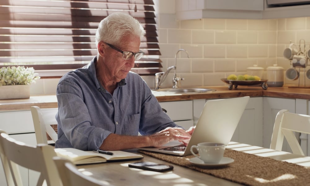 An elderly man working on his laptop in the kitchen