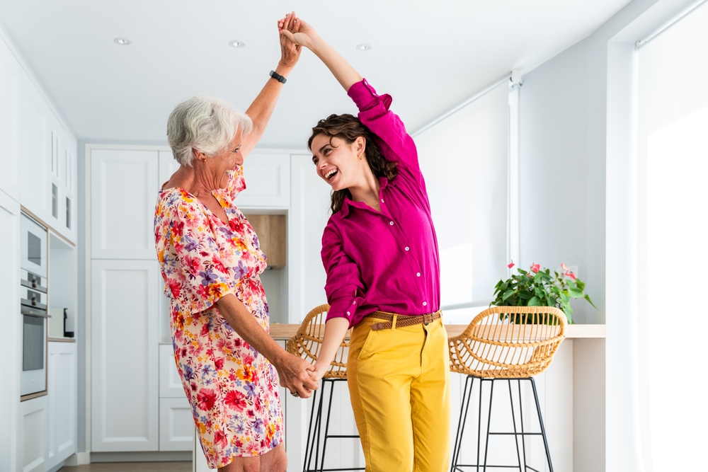Beautiful senior grandmother and granddaughter at home having fun and dancing together